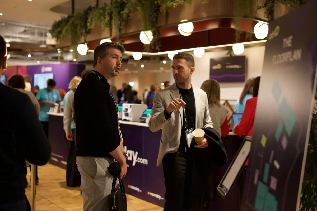 A partner talking with attendees beside the floor plan at aiblLIVE 2026